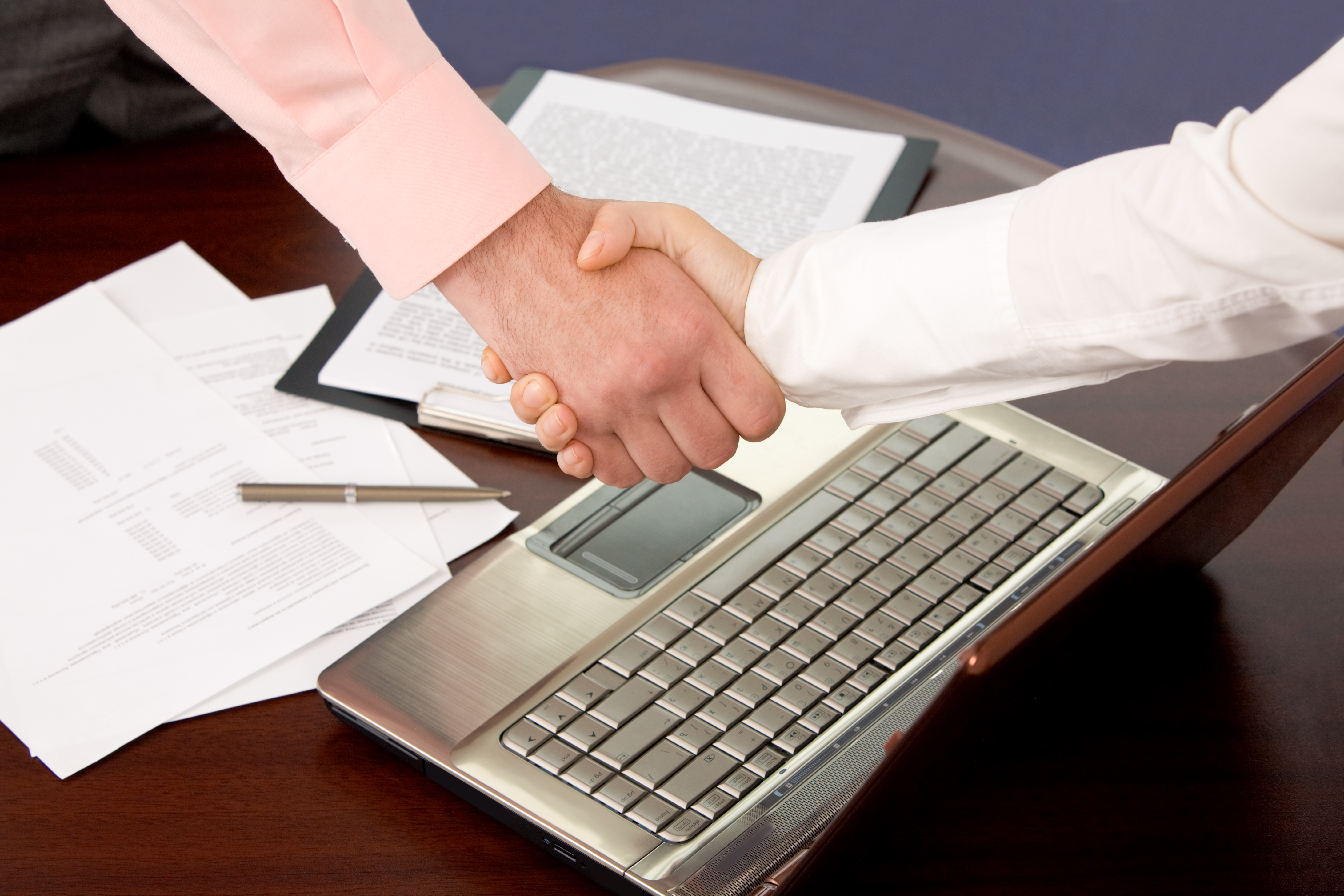 Shaking hands over a laptop on a desk